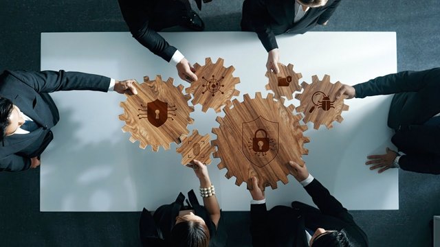 Collaboration in Cybersecurity: Diverse Professionals Linking Wooden Gears Embellished with Security Symbols and Icons in a Modern Office Environment. Amity