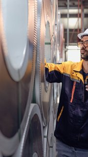 Latino engineer in safety helmet uniform working in heavy steel engineering factory. Hispanic technician manager worker using mobile inspecting metalwork product manufacturing facility workplace