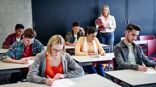 Group of college students in exam, teacher watching