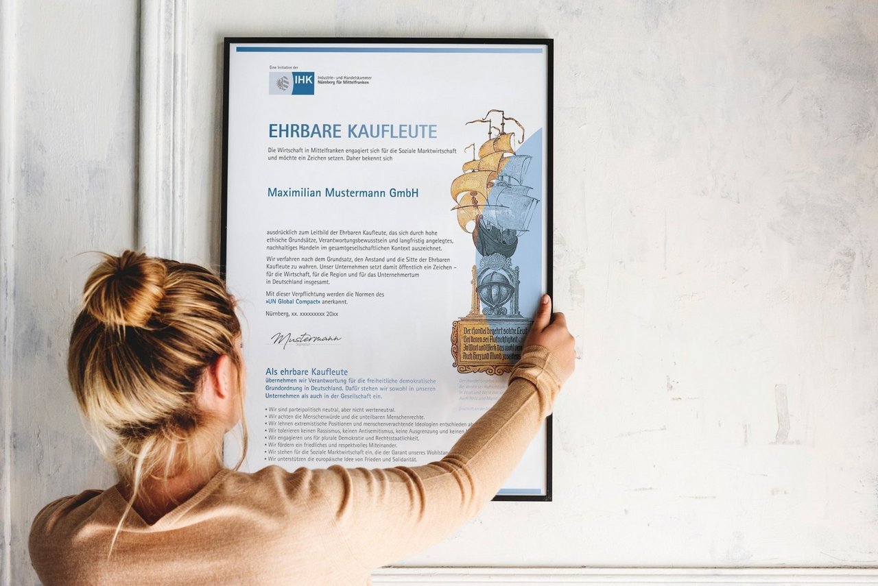 Eine Frau hängt die Urkunde "Ehrbare Kaufleute" an die Wand.