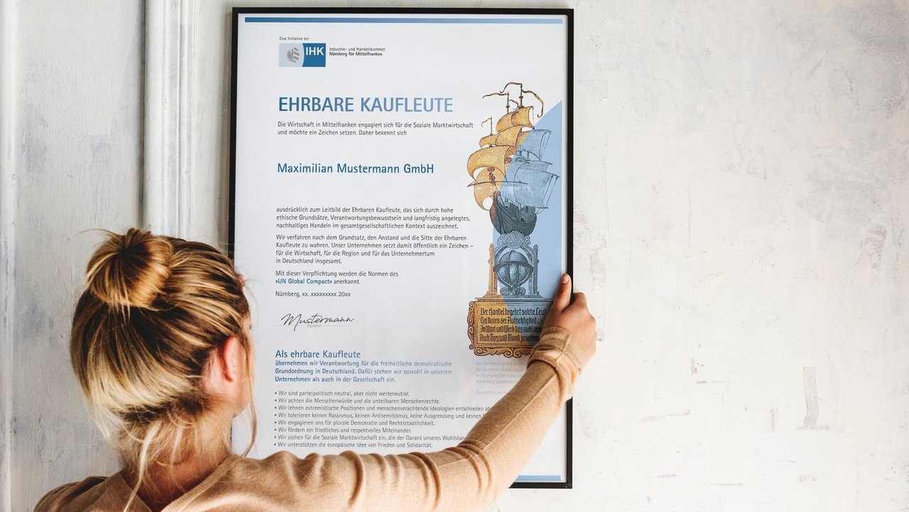 Eine Frau hängt die Urkunde "Ehrbare Kaufleute" an die Wand.