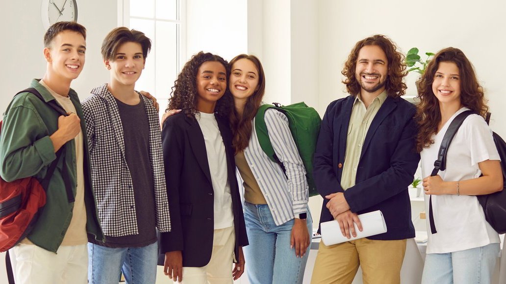 Happy smiling male teacher standing together with high school students in the classroom.