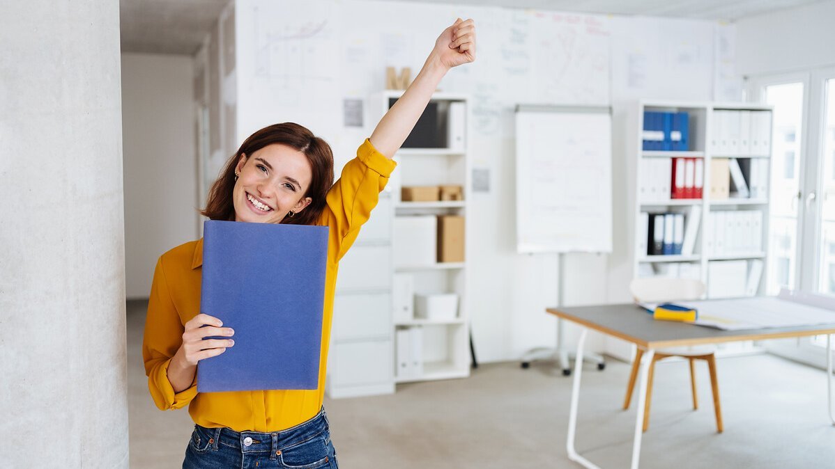 Young student stands in the office with her application documents and is happy about the new job