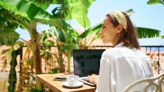 Young woman sitting on terrace at morning during vacation, using laptop computer