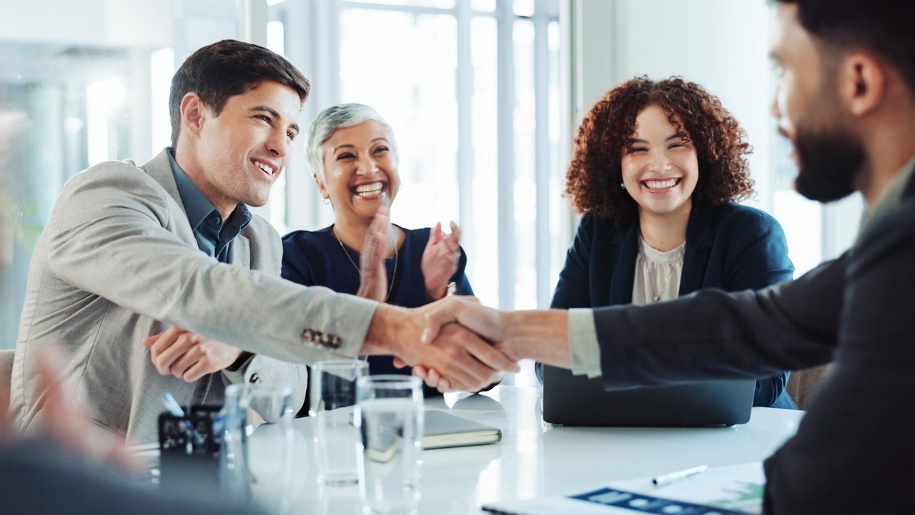 Happy, business people and applause with handshake for good deal, partnership or agreement at conference. Businessman, colleagues or employees shaking hands with team for introduction at workplace
