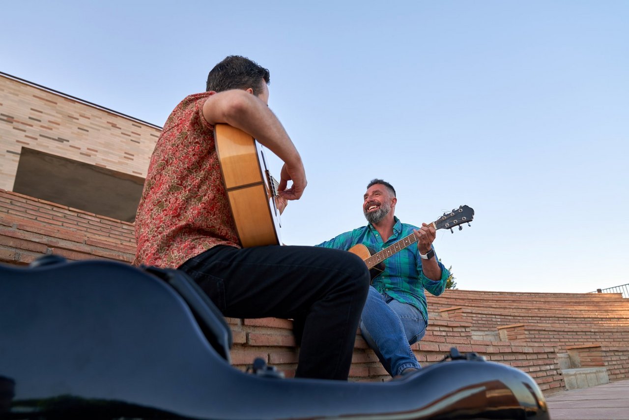Two lively men playing guitar together on stage at an open air amphitheater as the sun sets