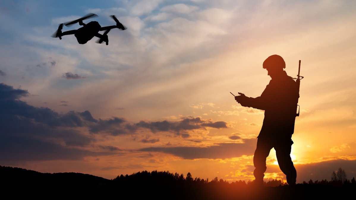 Silhouette eines Soldaten mit Drohne und Laptop vor dem Hintergrund eines Sonnenuntergangs.