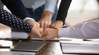 Team fists bumping gathered together at conference table